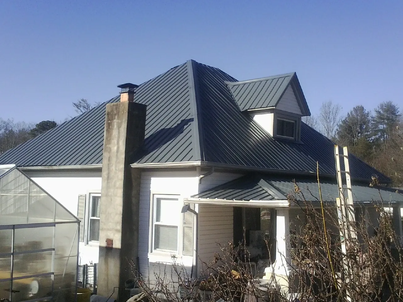 Dark blue standing seam metal roof on a white farmhouse with dormer — Slate & Tile Roof Repair by Roofing Brothers in West Newton
