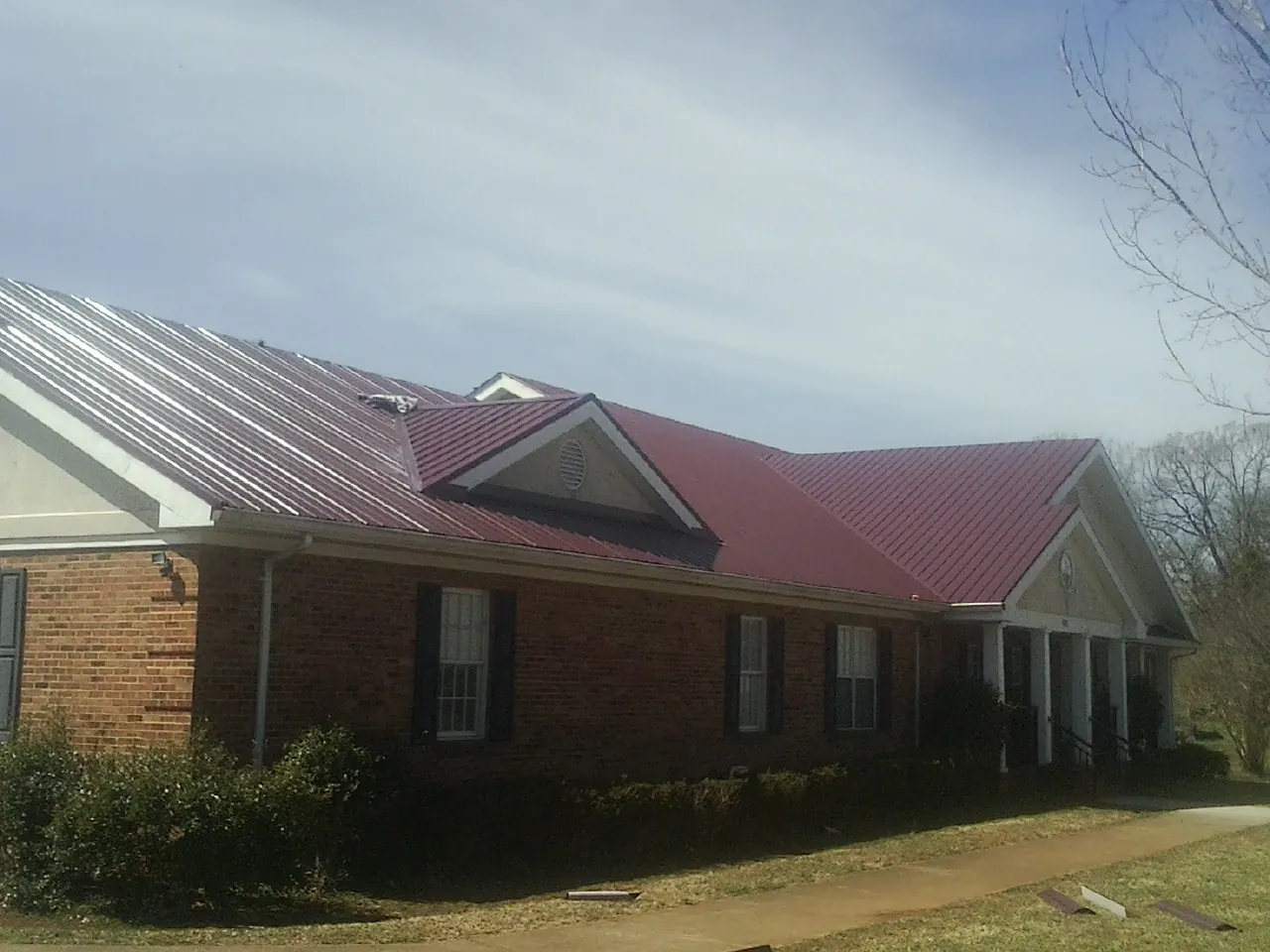 Red metal roof with gabled entries on a long brick building, from a Hail Damage Roof Repair job in West Newton