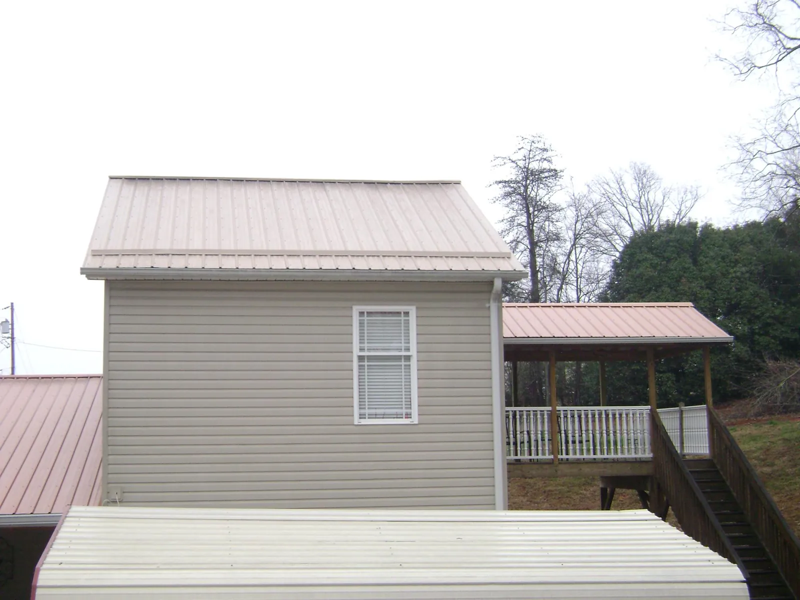 Tan metal roofs on a two story addition and attached porch, from a Roof Replacement job in West Newton